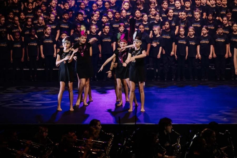 A group of young girls are dancing on a stage in front of a large audience.