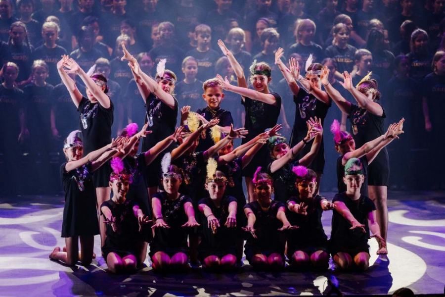 A group of children are dancing on a stage in front of a crowd.