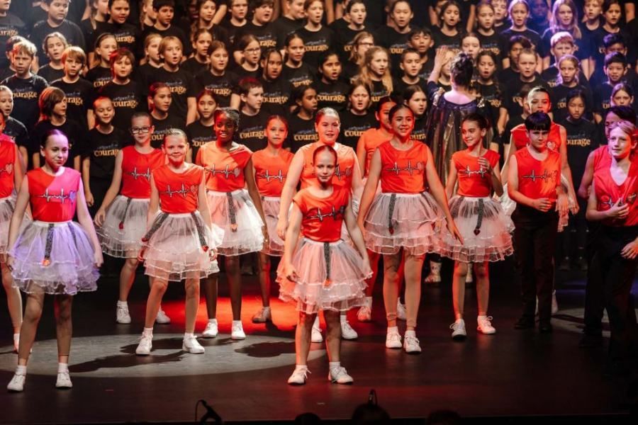A group of young girls are dancing on a stage in front of a large choir.