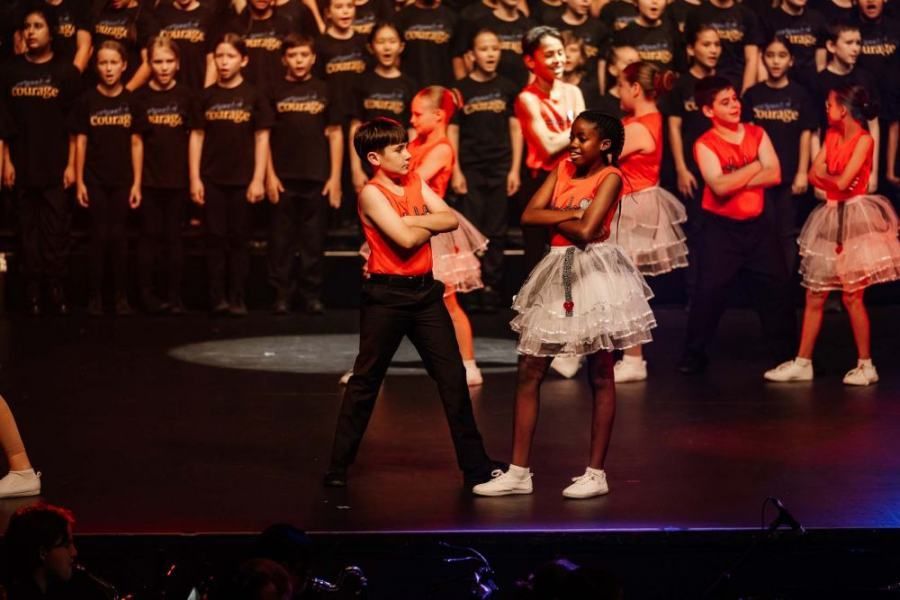 A group of children are dancing on a stage in front of a choir.