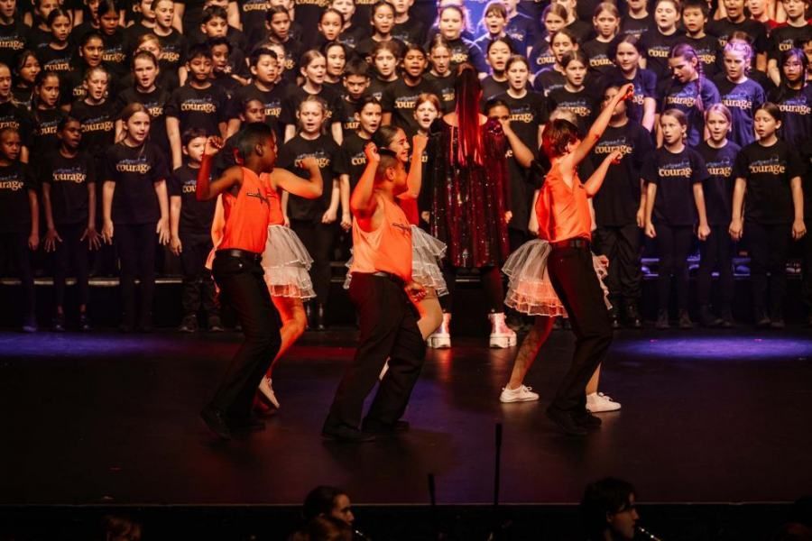 A group of children are dancing on a stage in front of a large choir.