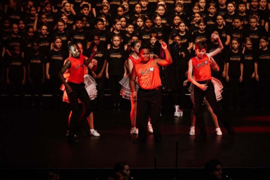 A group of people are dancing on a stage in front of a large audience.