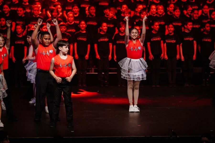 A group of children are dancing on a stage in front of a choir.