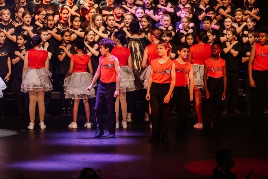A group of children are standing on a stage in front of a large choir.