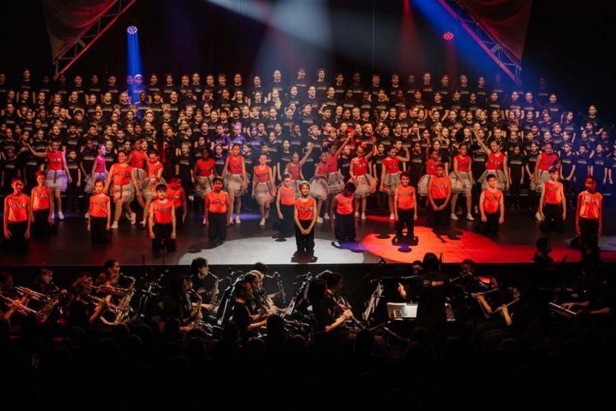 A large group of people are standing on a stage in front of an orchestra.
