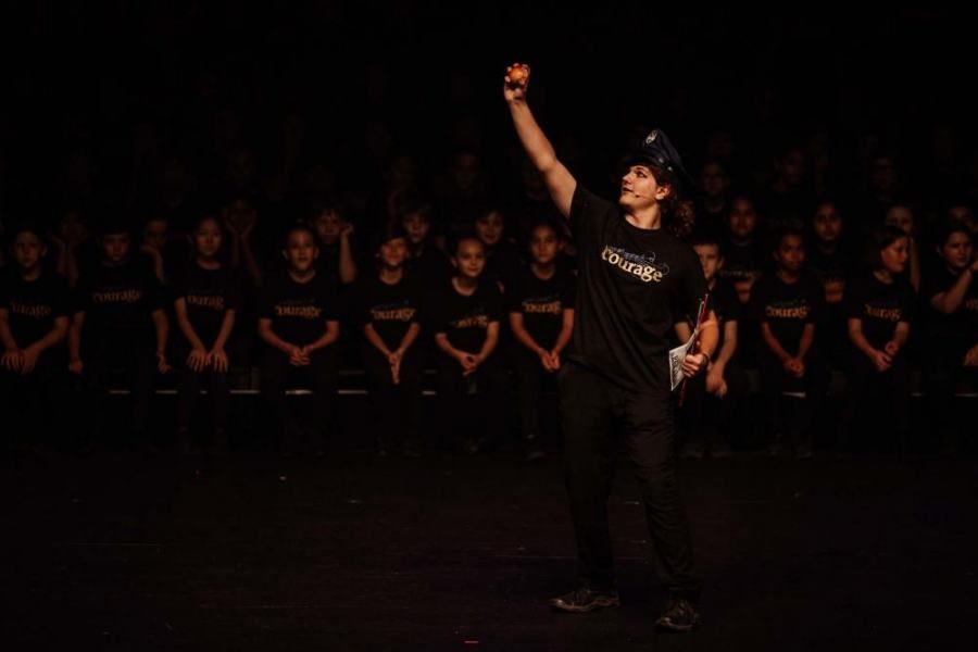 A man is standing on a stage holding a microphone in front of a crowd of people.
