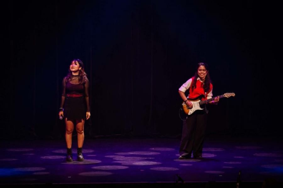 Two women are singing and playing guitar on a stage.