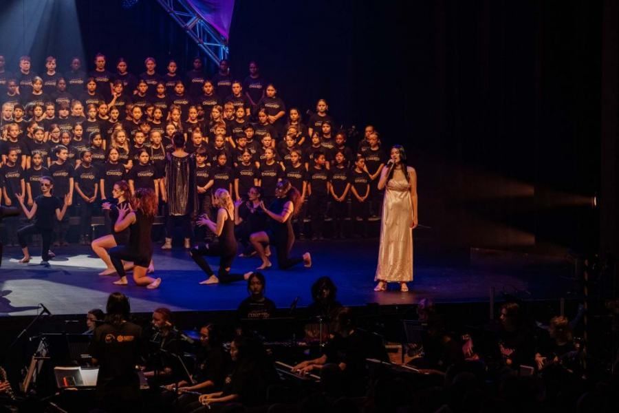 A woman is standing on a stage in front of a large choir.