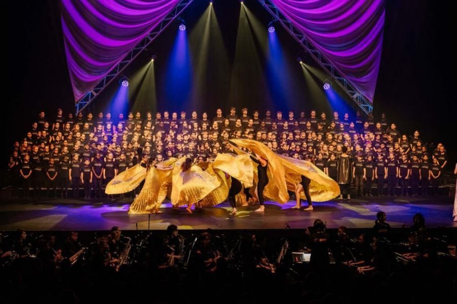 A large choir is performing on a stage in front of a crowd.