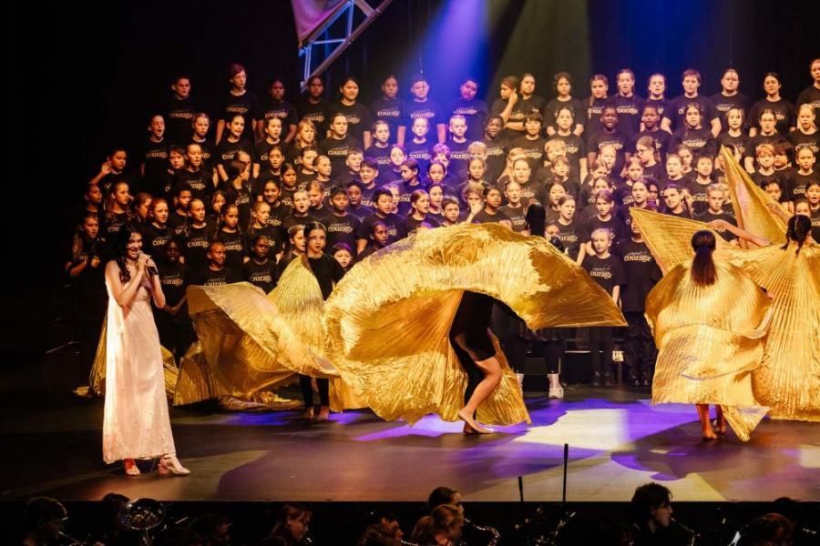 A woman is singing into a microphone on a stage in front of a choir.