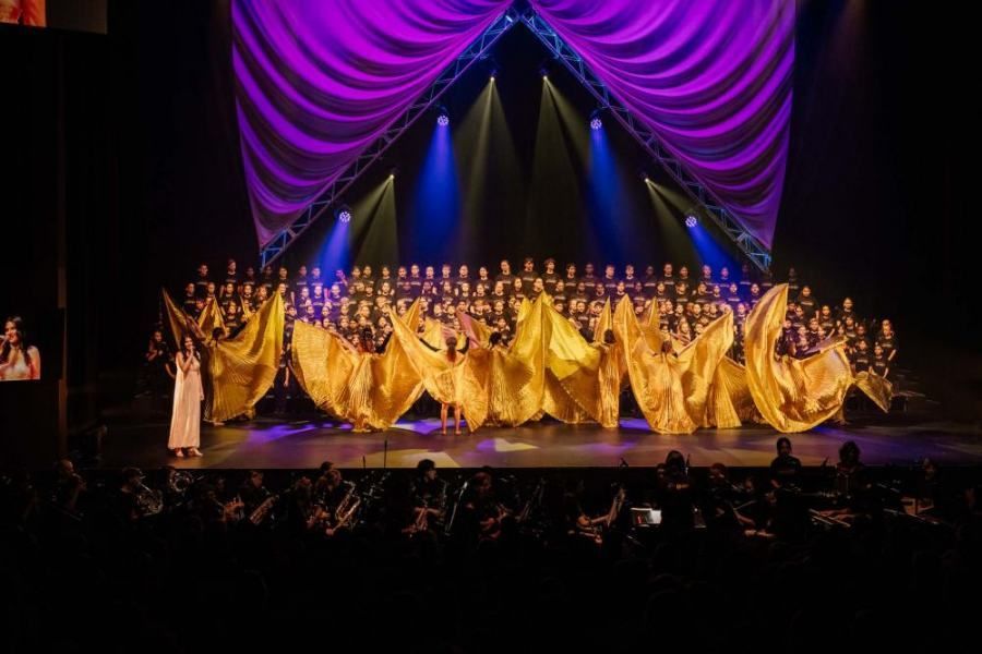A large choir is performing on a stage in front of a crowd.