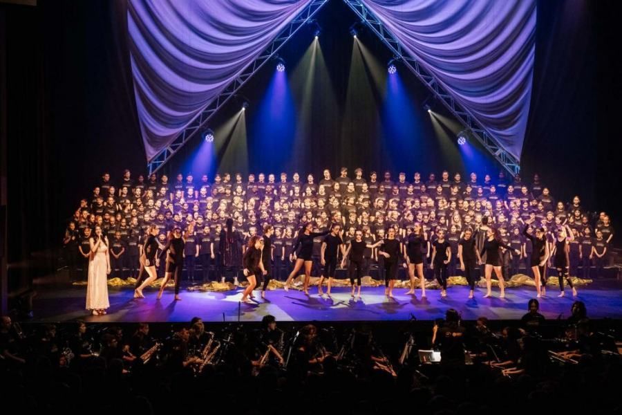 A large choir is performing on a stage in front of a crowd.
