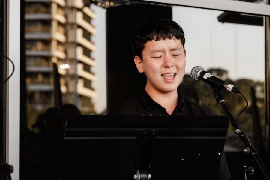 A young man is singing into a microphone while playing a keyboard.