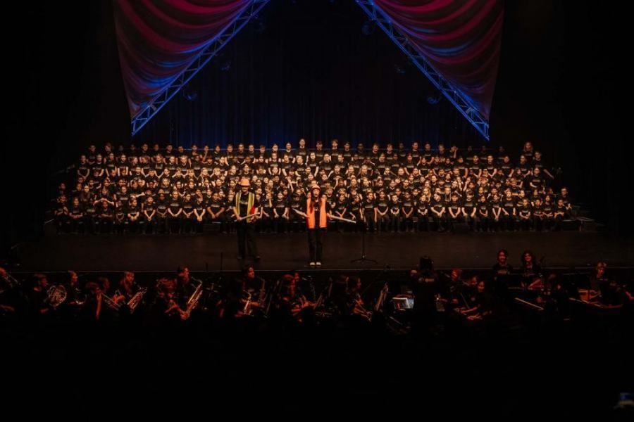 A large choir is performing on a stage in front of a crowd.