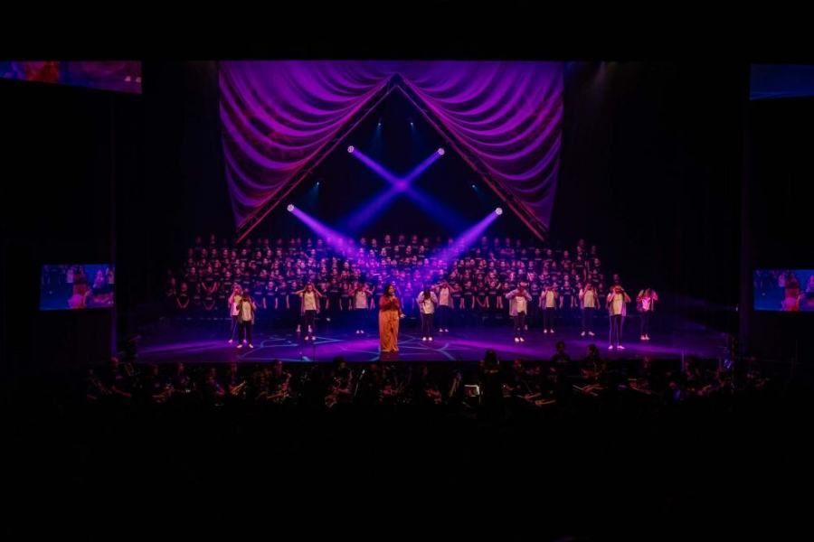 A woman is standing on a stage in front of a choir.