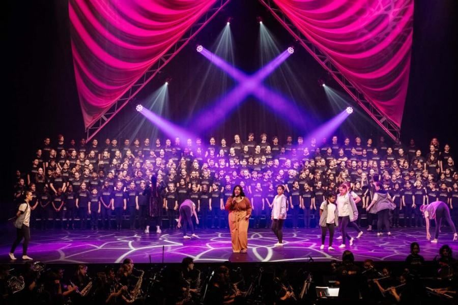 A woman is standing on a stage in front of a large choir.