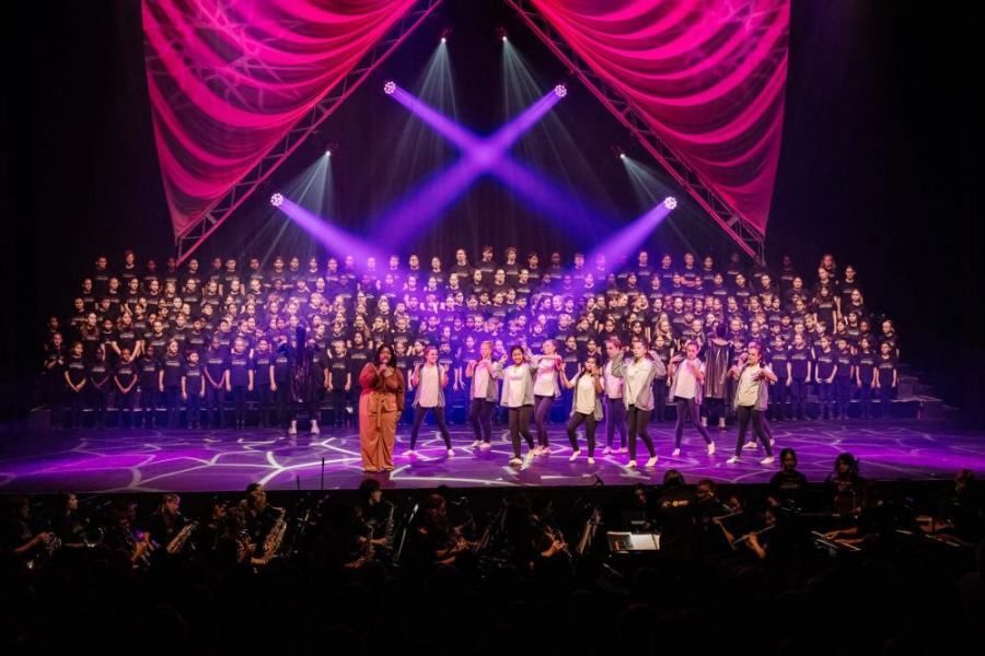 A large group of people are standing on a stage in front of a pink curtain.