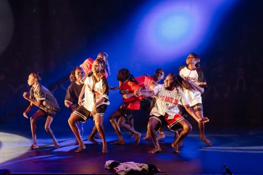 A group of people are dancing on a stage in front of a blue light.