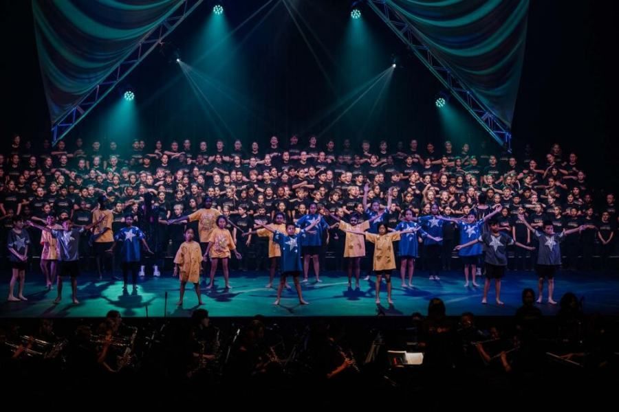 A large group of people are standing on a stage holding hands.