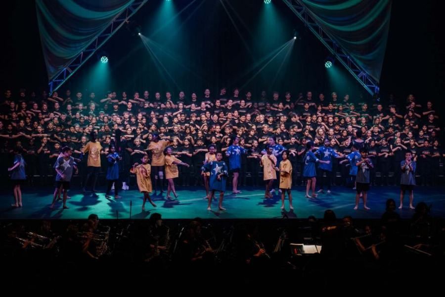 A large choir is performing on a stage in front of a crowd.