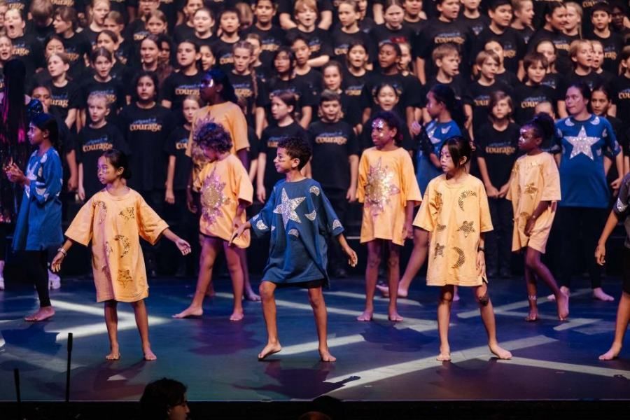 A large group of children are dancing on a stage