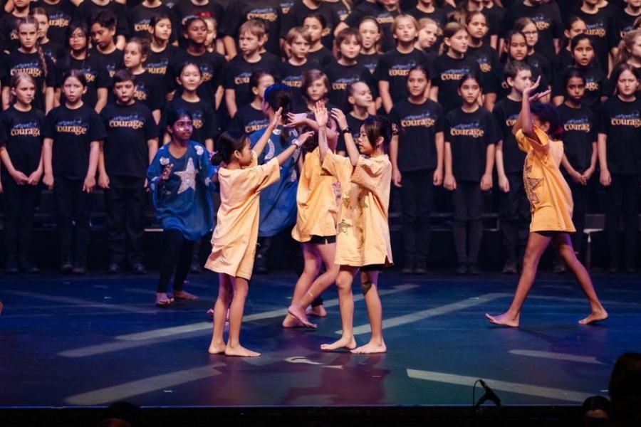 A group of young girls are dancing on a stage in front of a large choir