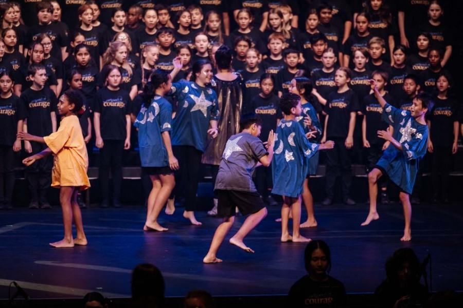 A group of children are dancing on a stage in front of a choir.