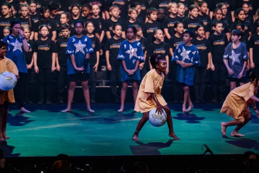 A group of children are playing soccer on a stage in front of a crowd.