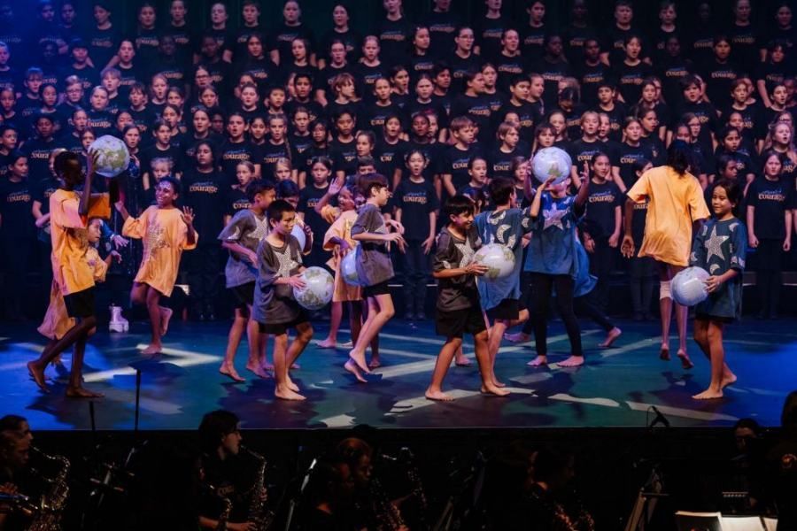 A group of children are dancing on a stage in front of a large choir.