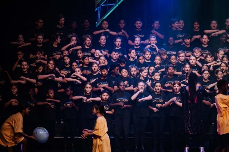 A large group of children are singing together on a stage.