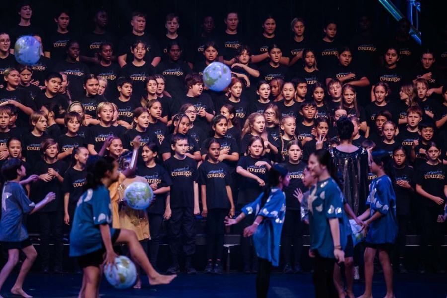 A large group of children are standing on a stage holding globe balloons.
