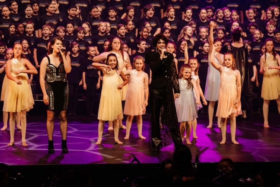A group of young girls are standing on a stage with a man singing into a microphone.