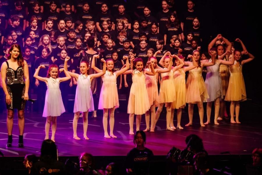 A group of young girls are standing on a stage holding hands.