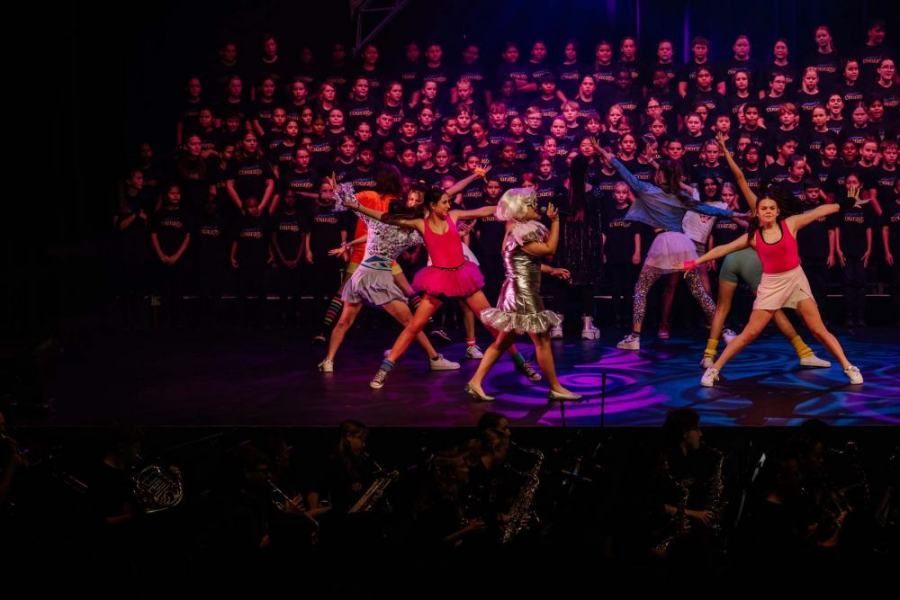 A group of young girls are dancing on a stage in front of a choir.
