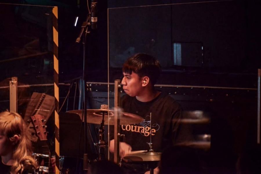 A man in a black shirt is playing drums in a dark room.