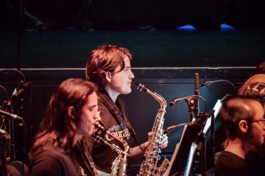 A man is playing a saxophone in an orchestra.