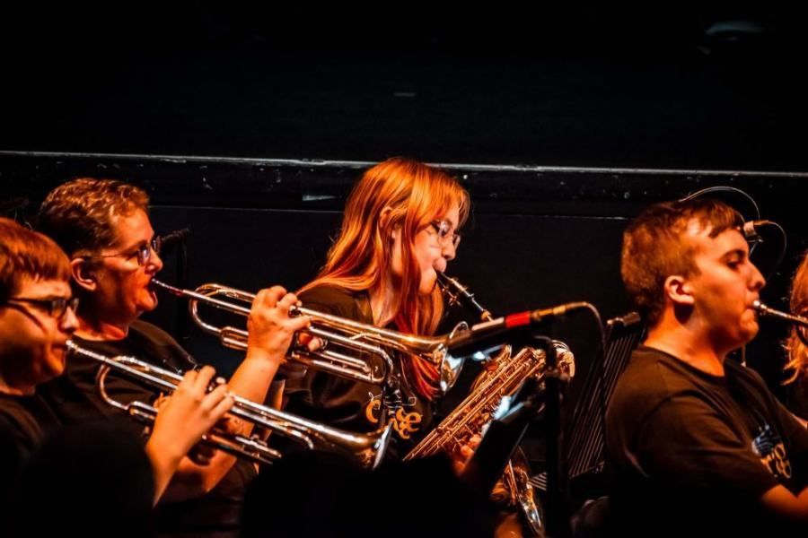 A group of people are playing trumpets and saxophones on a stage.
