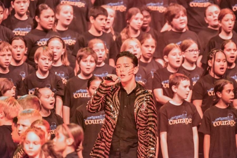 A man is singing into a microphone in front of a large choir.