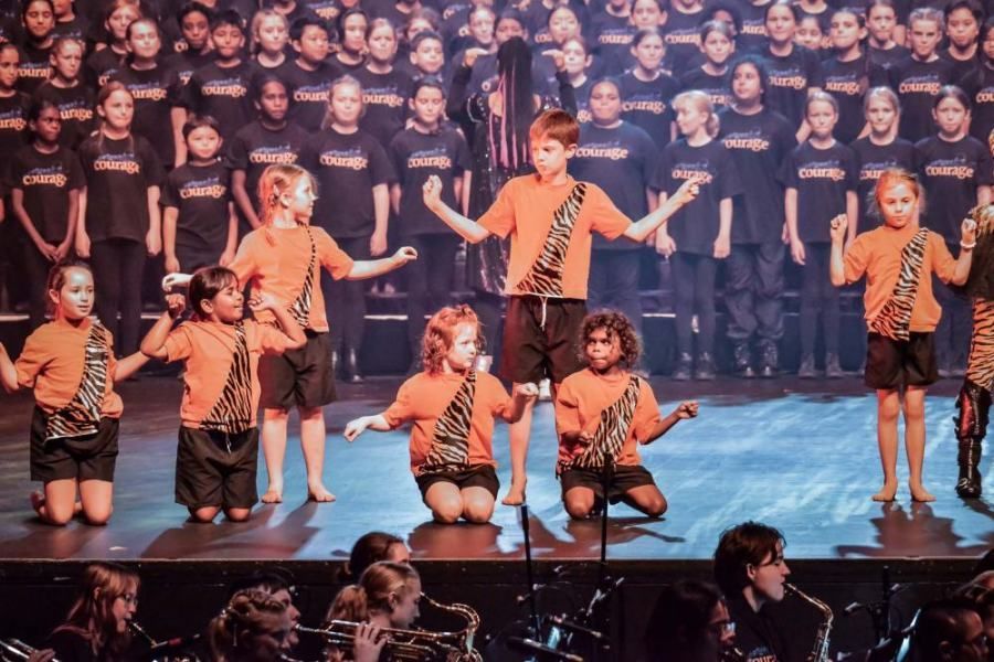 A group of children are singing in front of a large choir.