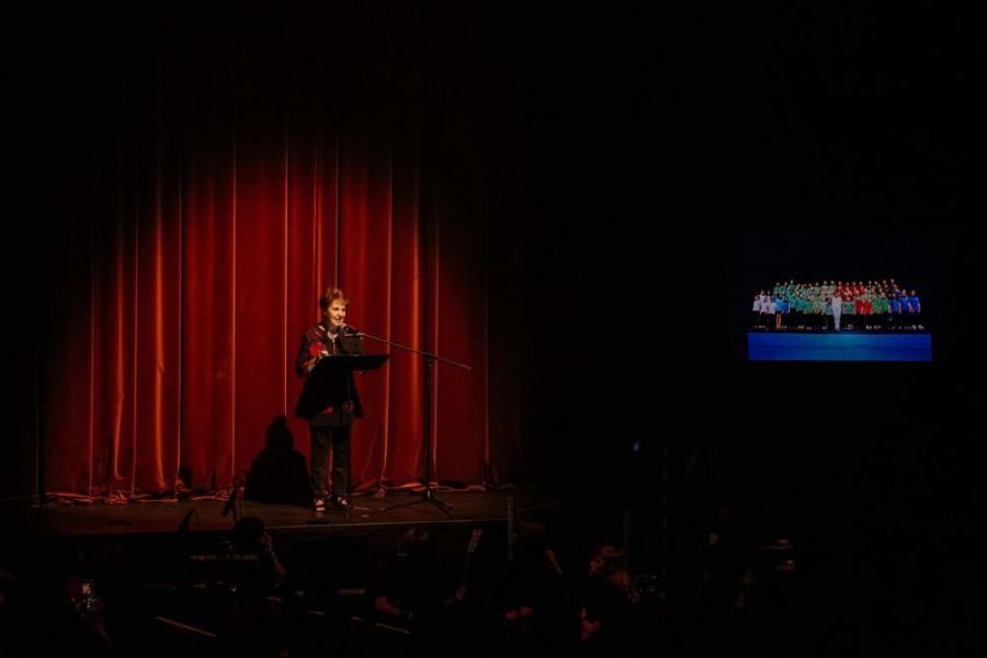 A woman is standing at a podium on a stage in front of a crowd.