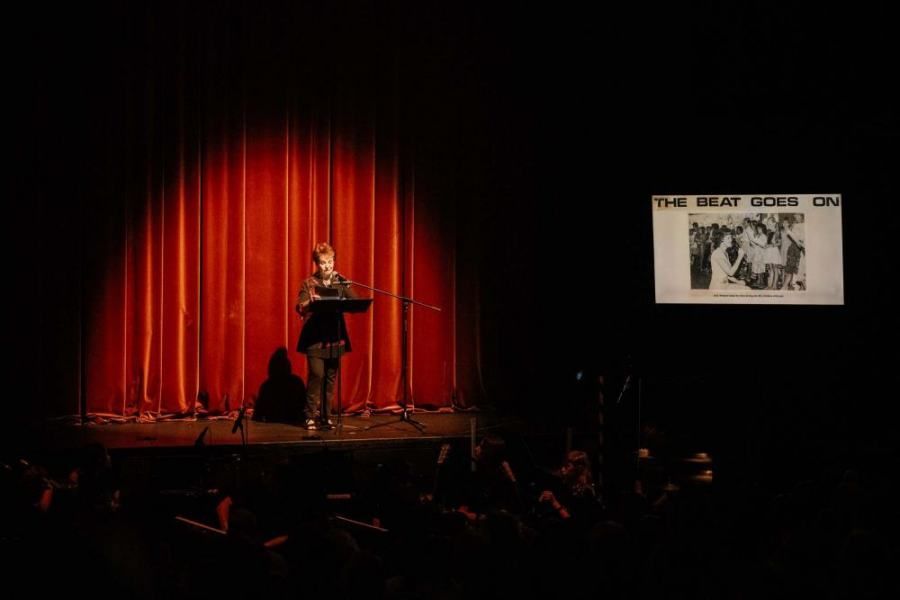 A woman is standing on a stage in front of a red curtain.