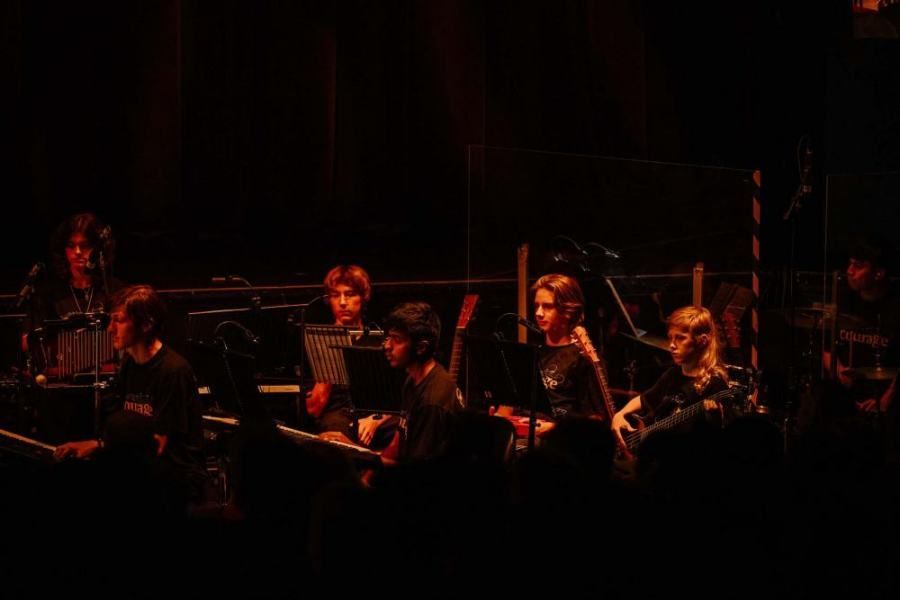A group of people are playing instruments on a stage in a dark room.