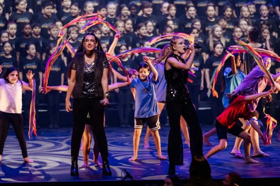 A group of children are dancing on a stage in front of a large choir.