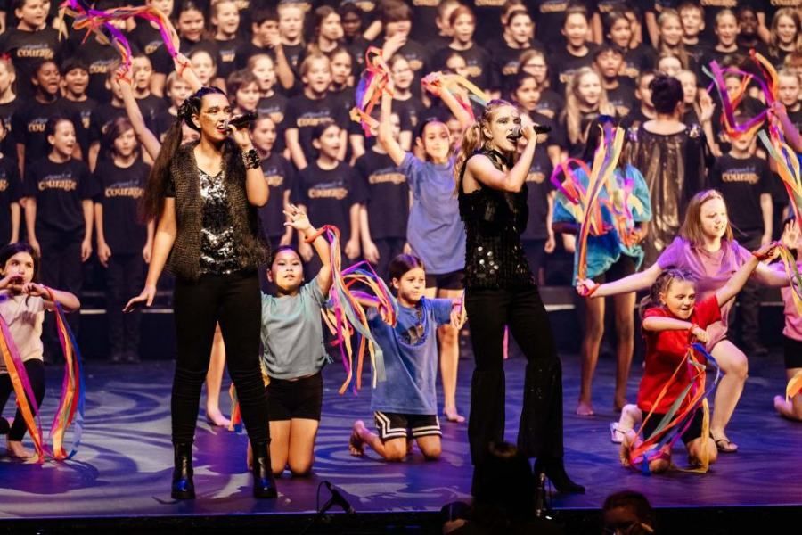 A group of children are dancing on a stage in front of a choir.