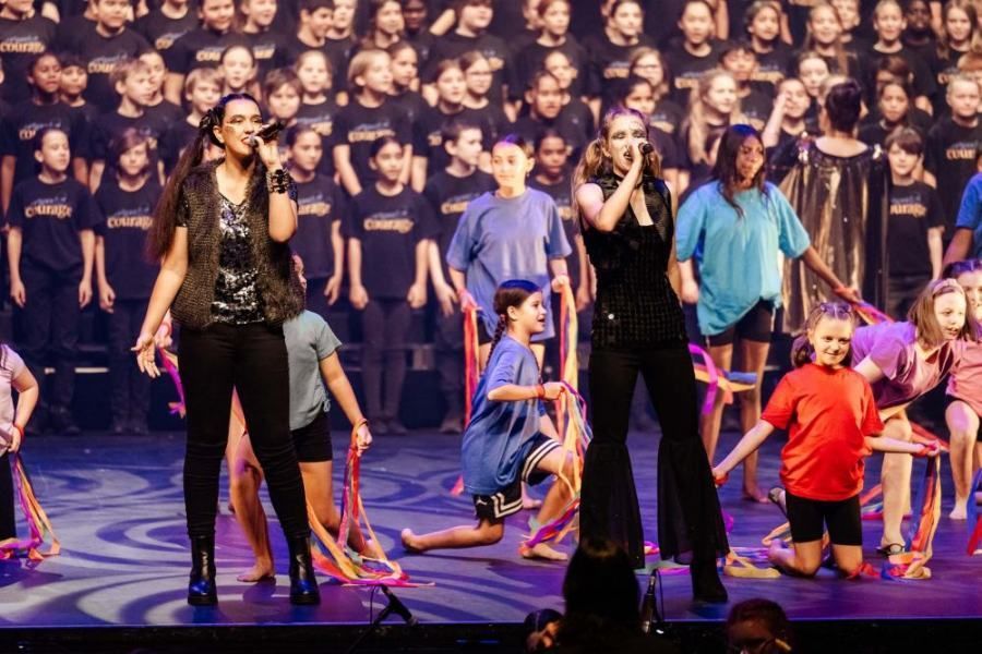 A group of children are performing on a stage in front of a large choir.