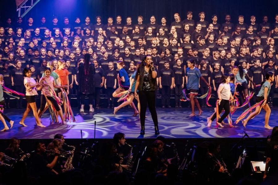 A woman is singing into a microphone on a stage in front of a large choir.