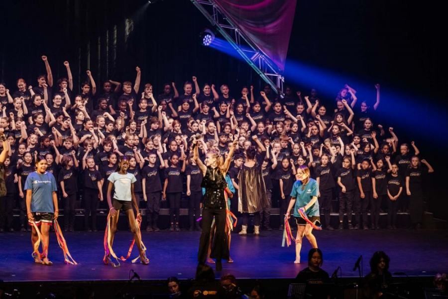 A large group of people are standing on a stage with their hands in the air.