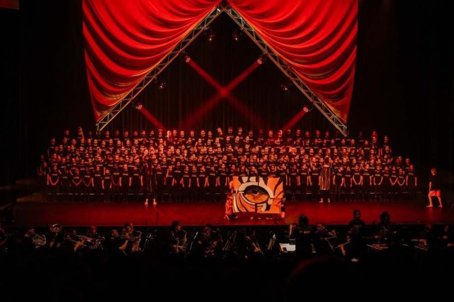 A large group of people are standing on a stage in front of a red curtain.
