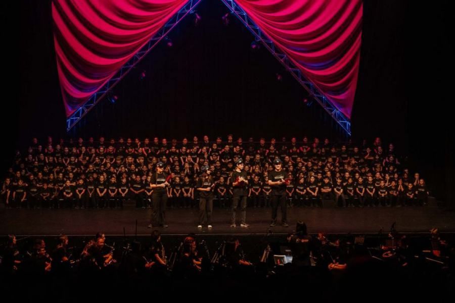 A large choir is standing on a stage in front of a red curtain.