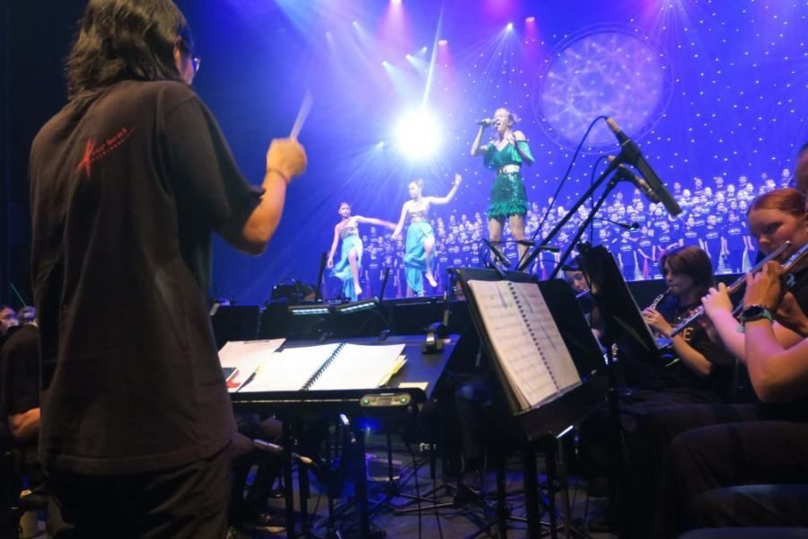A man in a black shirt is directing an orchestra on a stage